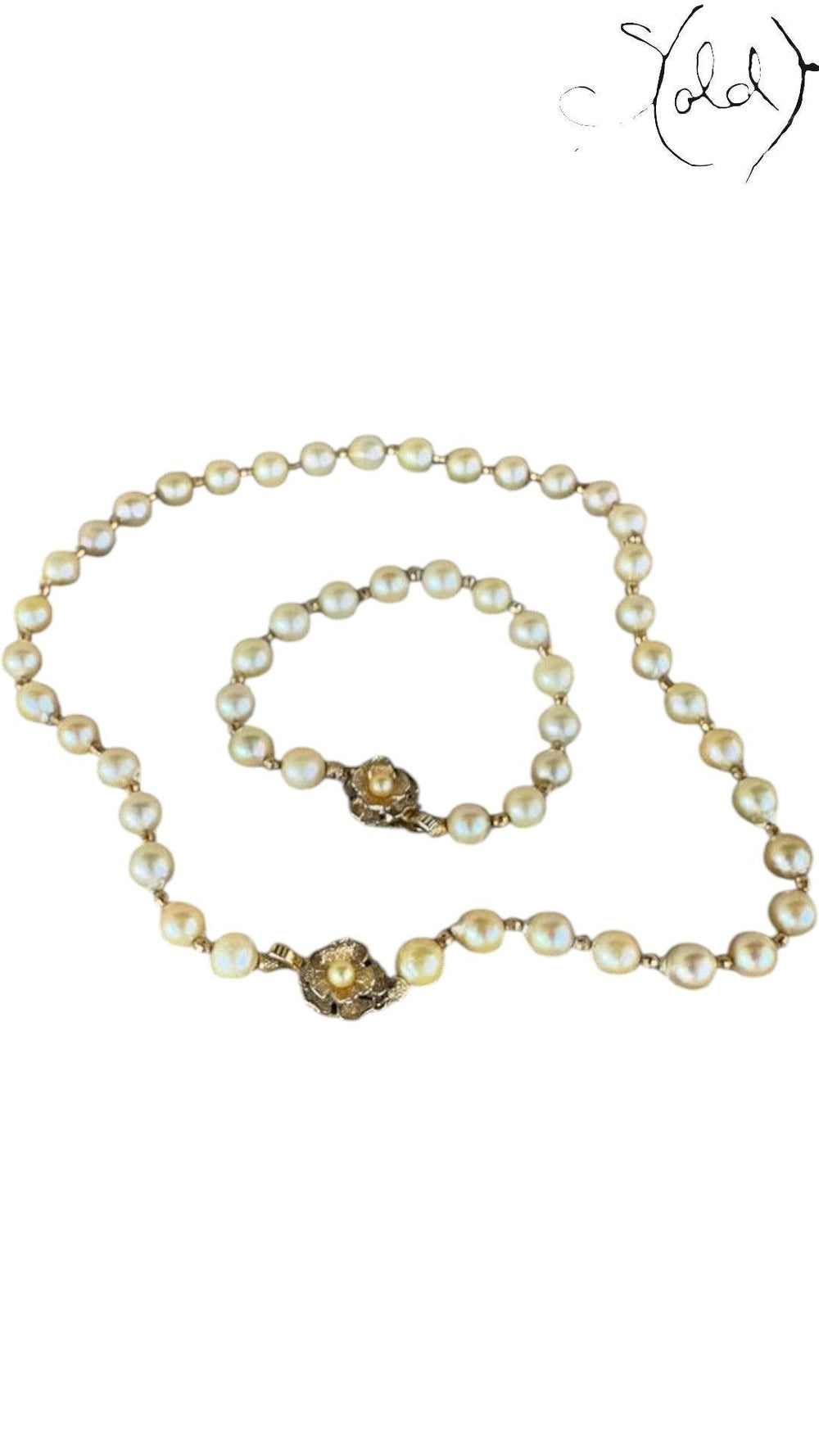 Sold Attire cream Akoya pearl necklace and bracelet set with decorative silver clasps on a patterned fabric background.