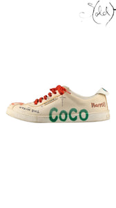 Sold Attire Chanel x Pharrell low-top sneakers in white canvas with green COCO lettering, red laces, and graphic print.