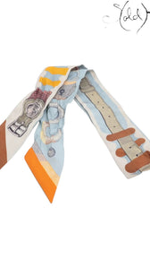 Sold Attire pre-owned Hermes Twilly silk ribbon scarf in light blue with orange and multicolor belt print design.
