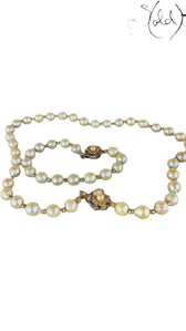 Sold Attire cream Akoya pearl necklace and bracelet set with decorative silver clasps on a patterned fabric background.
